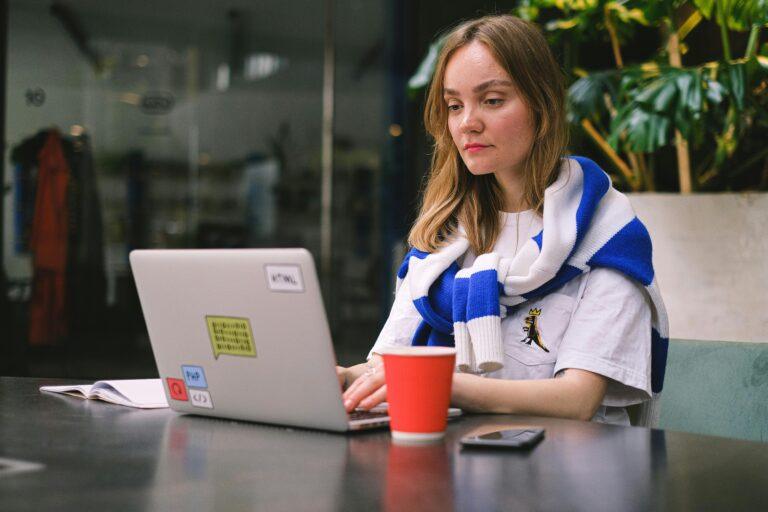 Young woman focused on laptop work in a modern cafe setting, surrounded by technology.